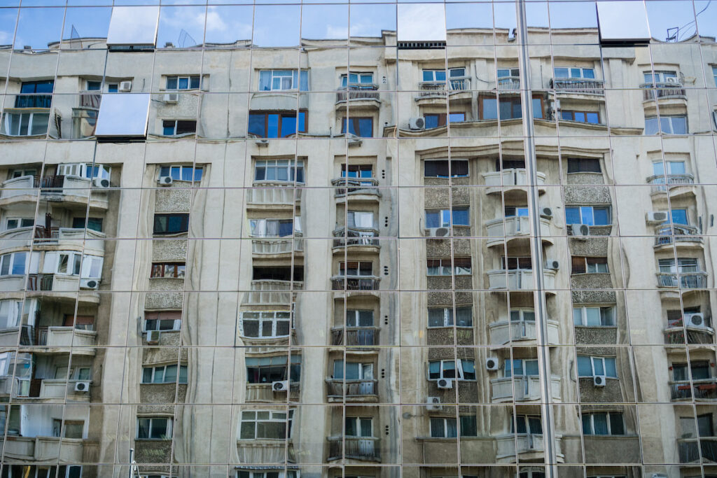 Distorted view of apartment building reflected in the glass facade of an office tower, Bucharest, Romania